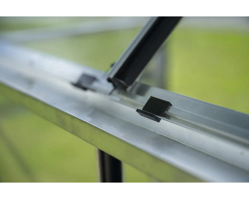 Detailansicht eines Gewächshauses mit Aluminiumrahmen und schwarzen Befestigungsklammern.