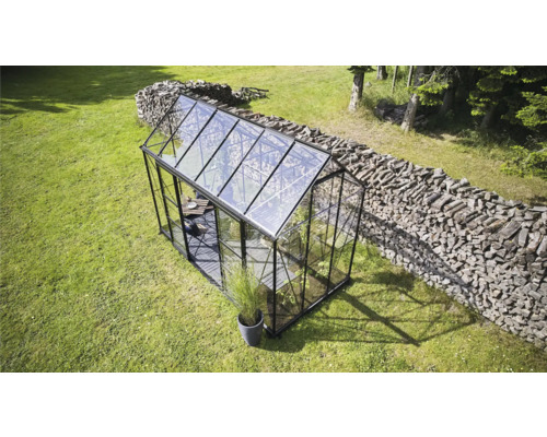 Serre sur une pelouse avec une pile de bois en arrière-plan.