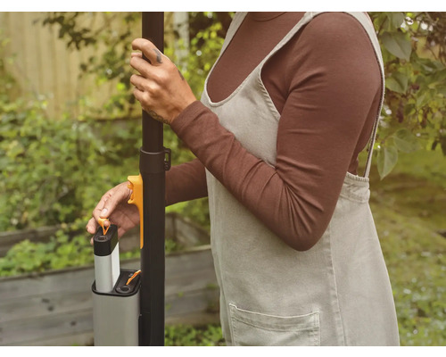 Une personne insère une batterie dans un outil de jardinage.