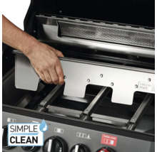 Une main place une plaque en acier inoxydable dans un barbecue.