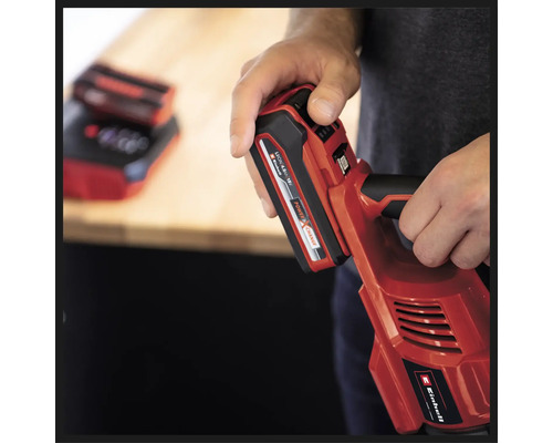 Une personne tient un outil sans fil rouge Einhell avec une batterie insérée.