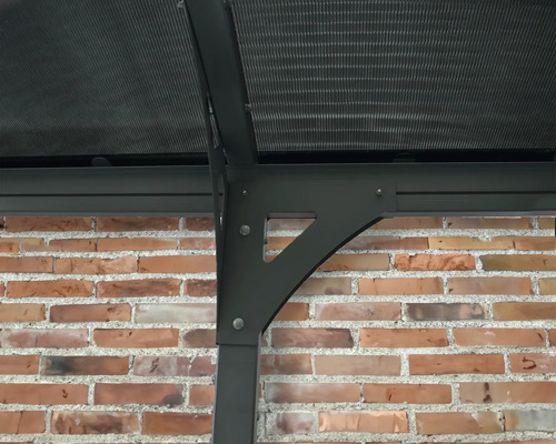 Detailansicht eines Pavillons mit Polycarbonatdach und einer Stützkonstruktion vor einer Ziegelwand