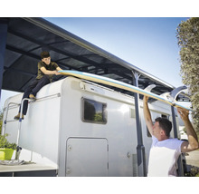 Deux personnes soulèvent une planche de surf sur un camping-car avec un store.