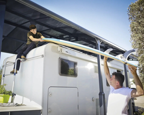 Deux personnes soulèvent une planche de surf sur un camping-car avec un store.