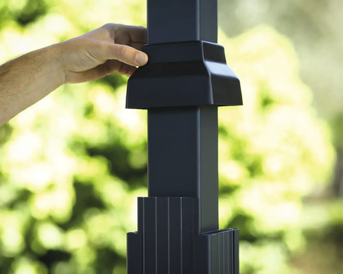 Main installant un capuchon de poteau noir sur un poteau de clôture