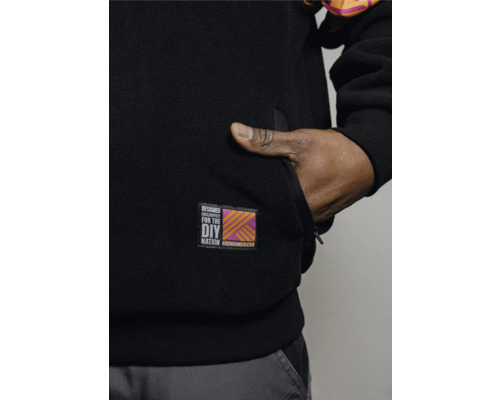 Detailaufnahme einer schwarzen Fleecejacke mit Hand in der Tasche und Hornbach DIY Nation Logo