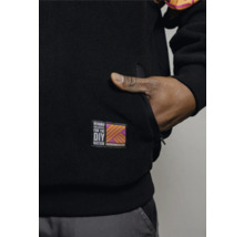 Détail d'une veste polaire noire avec un patch Hornbach DIY Nation et une main dans la poche