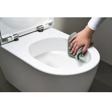 Une personne nettoie des toilettes suspendues blanches avec un chiffon.