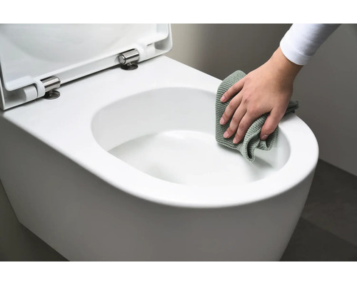 Une personne nettoie des toilettes suspendues blanches avec un chiffon.