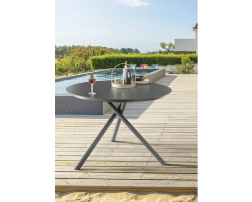 Table de jardin ronde sur une terrasse avec piscine et jardin en arrière-plan.