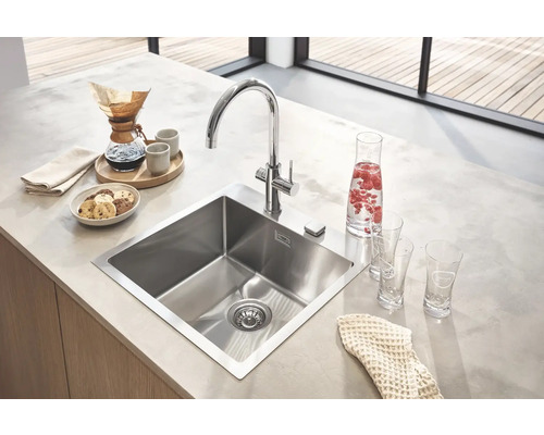 Küchenspüle aus Edelstahl mit Armatur auf einer Küchentheke mit Speisen und Getränken