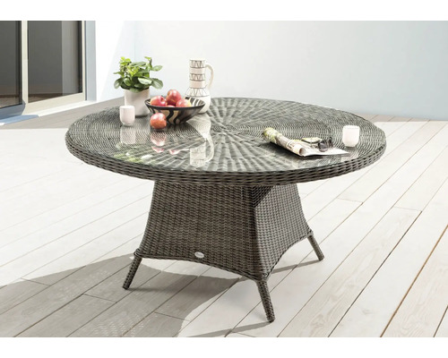 Table de jardin ronde avec plateau en verre et aspect rotin sur une terrasse.