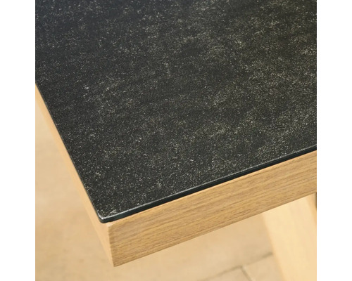 Gros plan sur un coin de table avec une surface sombre à l'aspect pierre et un cadre en décor bois clair.