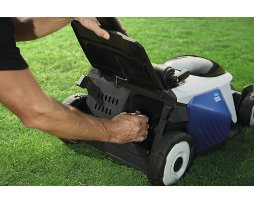 Ein Mann entleert den Fangkorb eines Rasenmähers auf einer Rasenfläche.
