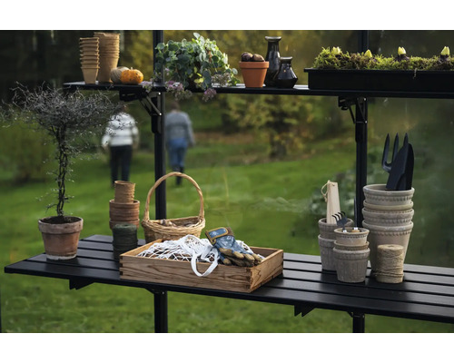 Scène de jardin avec table de plantation, pots, outils et plantes dans une serre