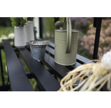 Gros plan d'une serre avec des étagères sur lesquelles sont posés un arrosoir, des pots et des vases.
