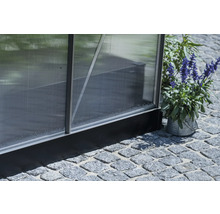 Vue détaillée d'une serre avec panneaux en polycarbonate et cadre en aluminium, posée sur un pavage en pierre.