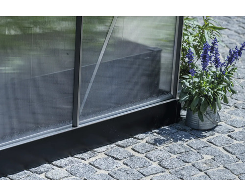 Vue détaillée d'une serre avec panneaux en polycarbonate et cadre en aluminium, posée sur un pavage en pierre.