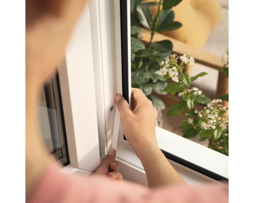 Une personne installe un joint de fenêtre sur un cadre de fenêtre blanc.