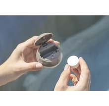 Les mains tiennent un distributeur rond avec un couvercle ouvert et un comprimé.