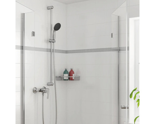 Modernes Duschset mit Handbrause, Mischbatterie und wandmontiertem Duschkorb auf weißen Fliesen mit Mosaikbordüre.