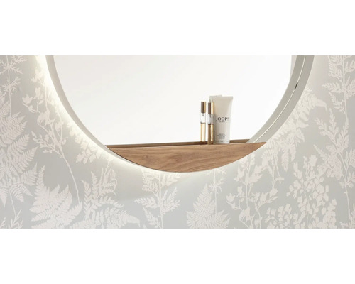 Miroir mural rond avec éclairage LED intégré et étagère incurvée en bois devant un mur au motif de fougères.