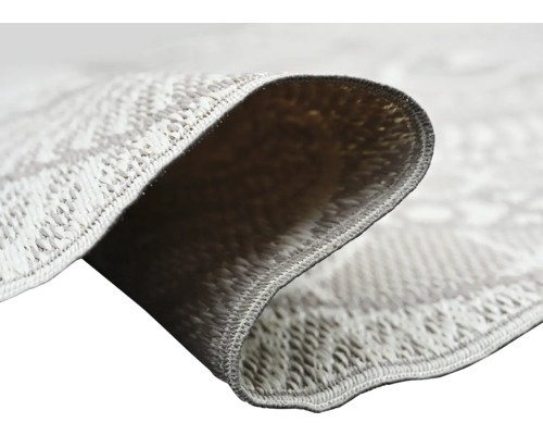 Gros plan d'un tapis à tissage plat avec motif géométrique montrant la structure du tissage et l'envers du coin replié.