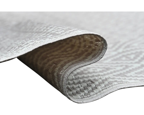 Nahaufnahme eines flachgewebten Teppichs mit geometrischem Muster, umgeschlagene Ecke zeigt die Struktur des Gewebes.