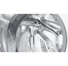 Gros plan d'un tambour de lave-linge en acier inoxydable avec perforations et vue à travers la porte ouverte.