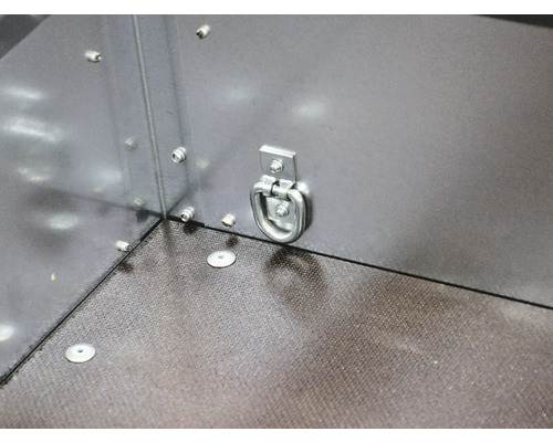 Anneau d'arrimage en métal sur une paroi latérale de remorque pour sécuriser le chargement au-dessus d'un sol structuré.