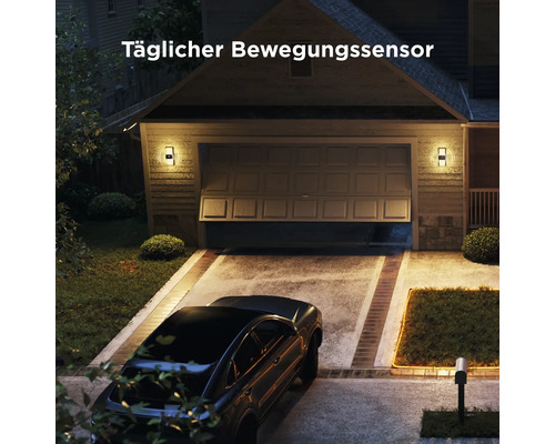 Wandleuchten mit Bewegungssensor an einer Garage bei Nacht, hell beleuchtete Einfahrt mit geparktem Auto und Text Täglicher Bewegungssensor.
