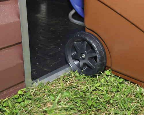 Roue en plastique Biohort d un système de roulement franchissant le seuil d un abri de jardin au-dessus de l herbe.