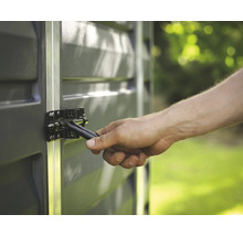 Gros plan d'une main actionnant un verrou métallique noir sur un abri de jardin gris avec des profilés en aluminium.