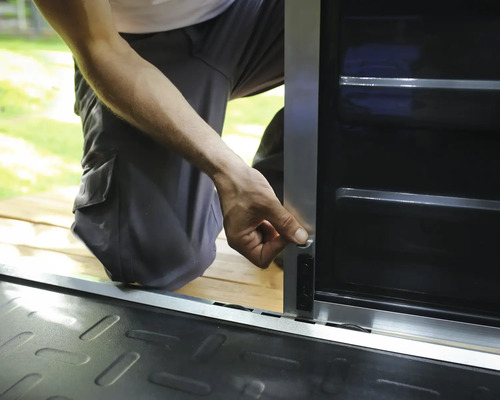 Personne installant un verrou sur une armoire de rangement en métal avec un cadre argenté et des panneaux noirs.