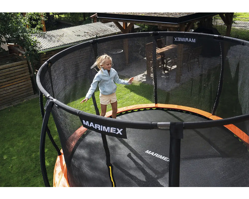 Ein Kind springt auf einem runden Marimex Gartentrampolin mit schwarzem Sicherheitsnetz und orangefarbenem Randschutz in einem Garten.