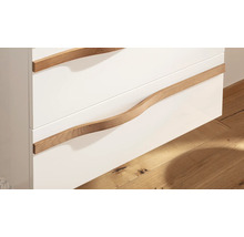 Gros plan d'un meuble de salle de bain avec des façades de tiroirs blanches et des poignées courbées en bois.