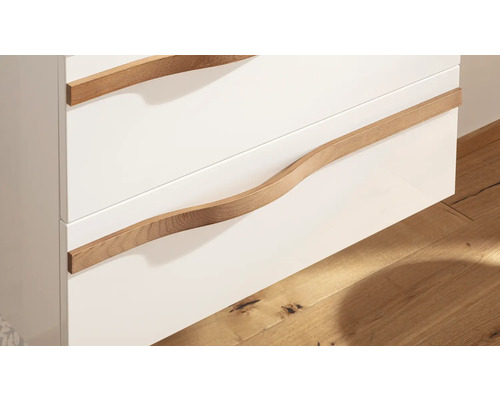 Gros plan d'un meuble de salle de bain avec des façades de tiroirs blanches et des poignées courbées en bois.