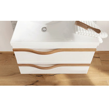 Meuble sous-vasque blanc avec deux tiroirs, poignées en bois ondulées et lavabo intégré sur sol en bois.