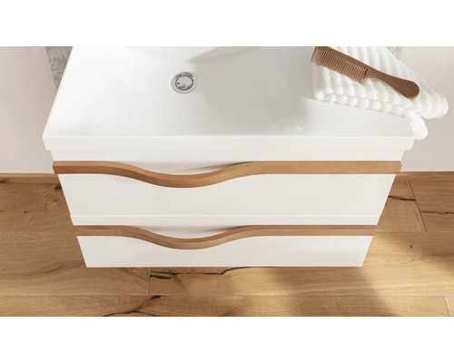 Meuble sous-vasque blanc avec deux tiroirs, poignées en bois ondulées et lavabo intégré sur sol en bois.