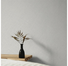 Papier peint intissé avec une fine structure de lin sur un mur derrière un vase avec une feuille séchée sur une table en bois.