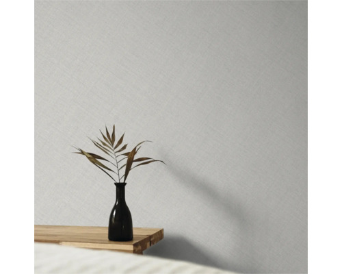 Papier peint intissé avec une fine structure de lin sur un mur derrière un vase avec une feuille séchée sur une table en bois.