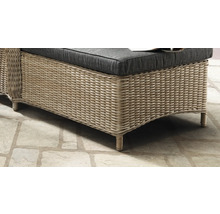 Détail de meuble de jardin en polyrotin avec coussin foncé sur un sol en pierre.