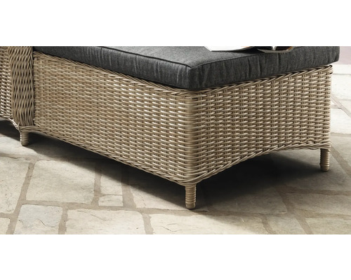 Détail de meuble de jardin en polyrotin avec coussin foncé sur un sol en pierre.