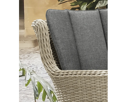 Détail d'un fauteuil de jardin en polyrotin tressé beige avec un coussin gris.