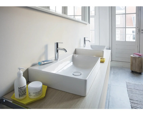 Modernes Badezimmer mit zwei rechteckigen Aufsatzwaschbecken aus weißer Keramik und verchromten Armaturen auf einer hellen Waschtischplatte.