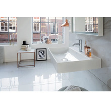 Modernes, helles Badezimmer mit wandhängendem, rechteckigem Keramik-Waschtisch, Chromarmatur und Fliesen in Marmoroptik.