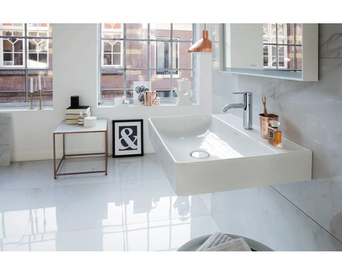 Modernes, helles Badezimmer mit wandhängendem, rechteckigem Keramik-Waschtisch, Chromarmatur und Fliesen in Marmoroptik.
