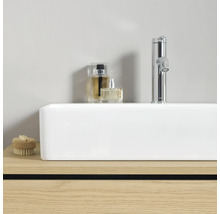 Weißes rechteckiges Aufsatzwaschbecken auf Holzunterschrank mit verchromter Armatur und Badzubehör in modernem, hellem Ambiente.