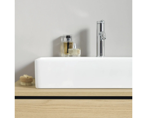 Weißes rechteckiges Aufsatzwaschbecken auf Holzunterschrank mit verchromter Armatur und Badzubehör in modernem, hellem Ambiente.