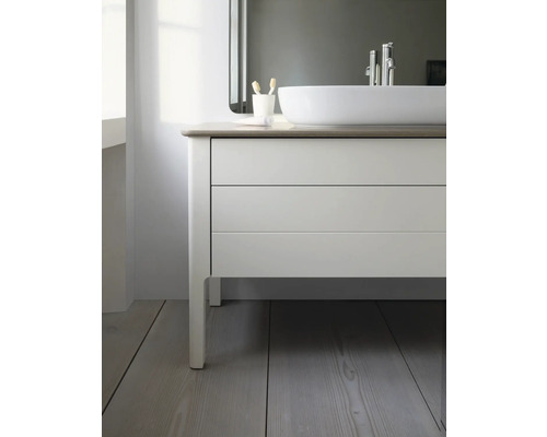 Moderner Badunterschrank mit hellen Fronten, zwei Auszügen und Aufsatzwaschbecken auf einem Holzfußboden in einem hellen Badezimmer.